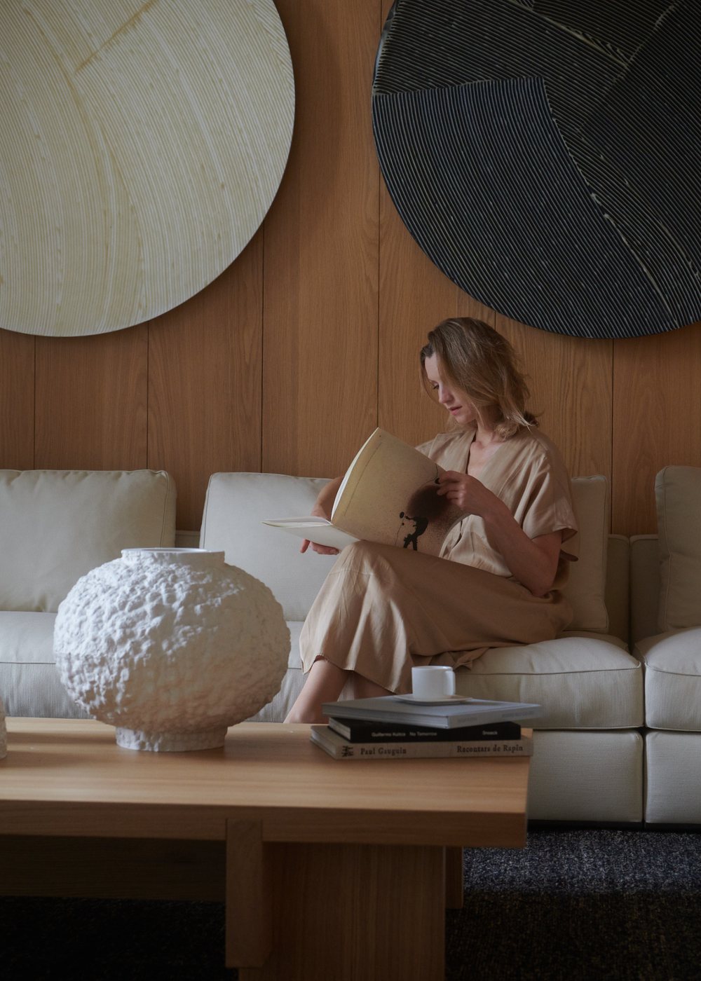 Anna Yermakova reading in a calm interior with sculptural vessels and circular wall works