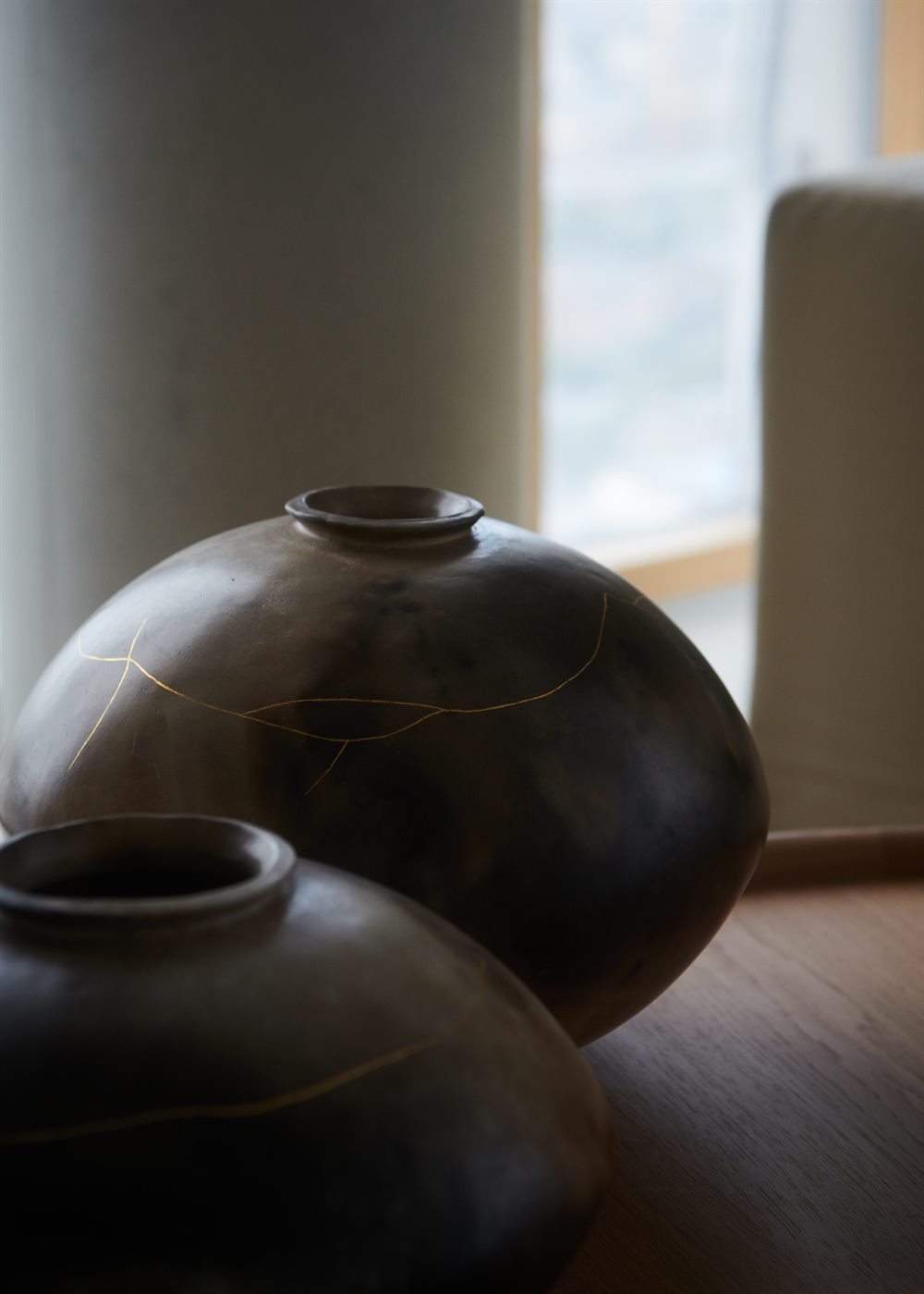 Dark ceramic vessels with fine gold line details beside a window